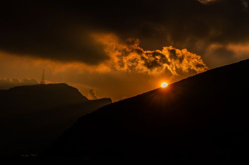 Free Capture of a dramatic sunset over silhouetted mountains with glowing clouds. Stock Photo