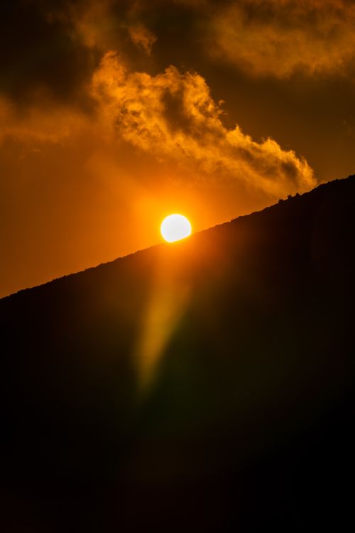 Free A stunning sunset with the sun peeking over a mountain silhouette, casting warm hues. Stock Photo