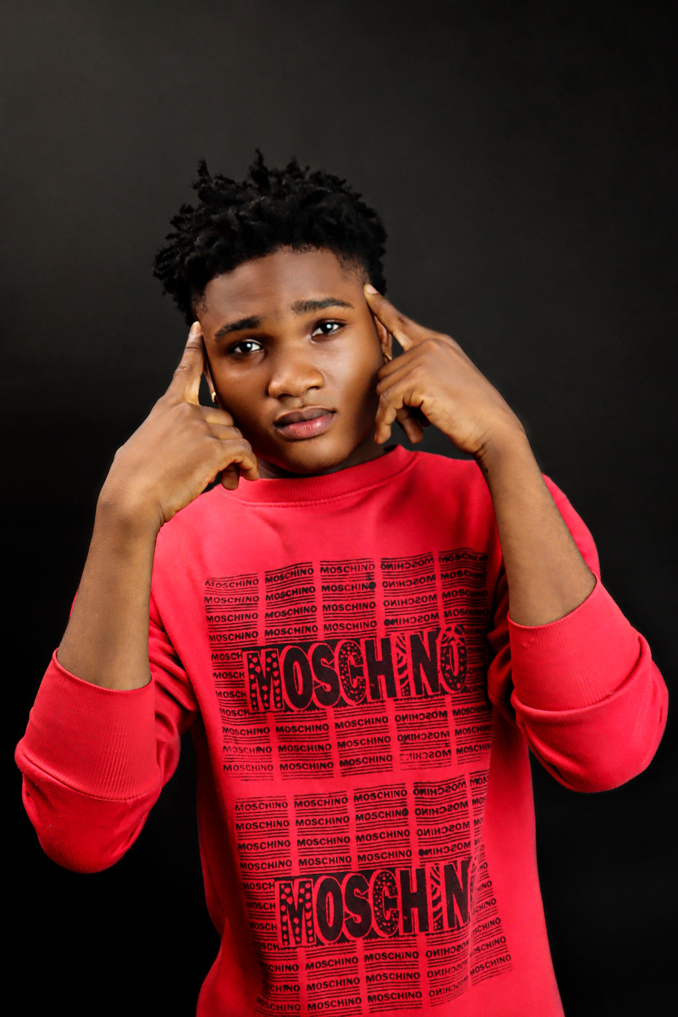 Portrait of a fashionable young man in a red sweater posing thoughtfully against a dark background.