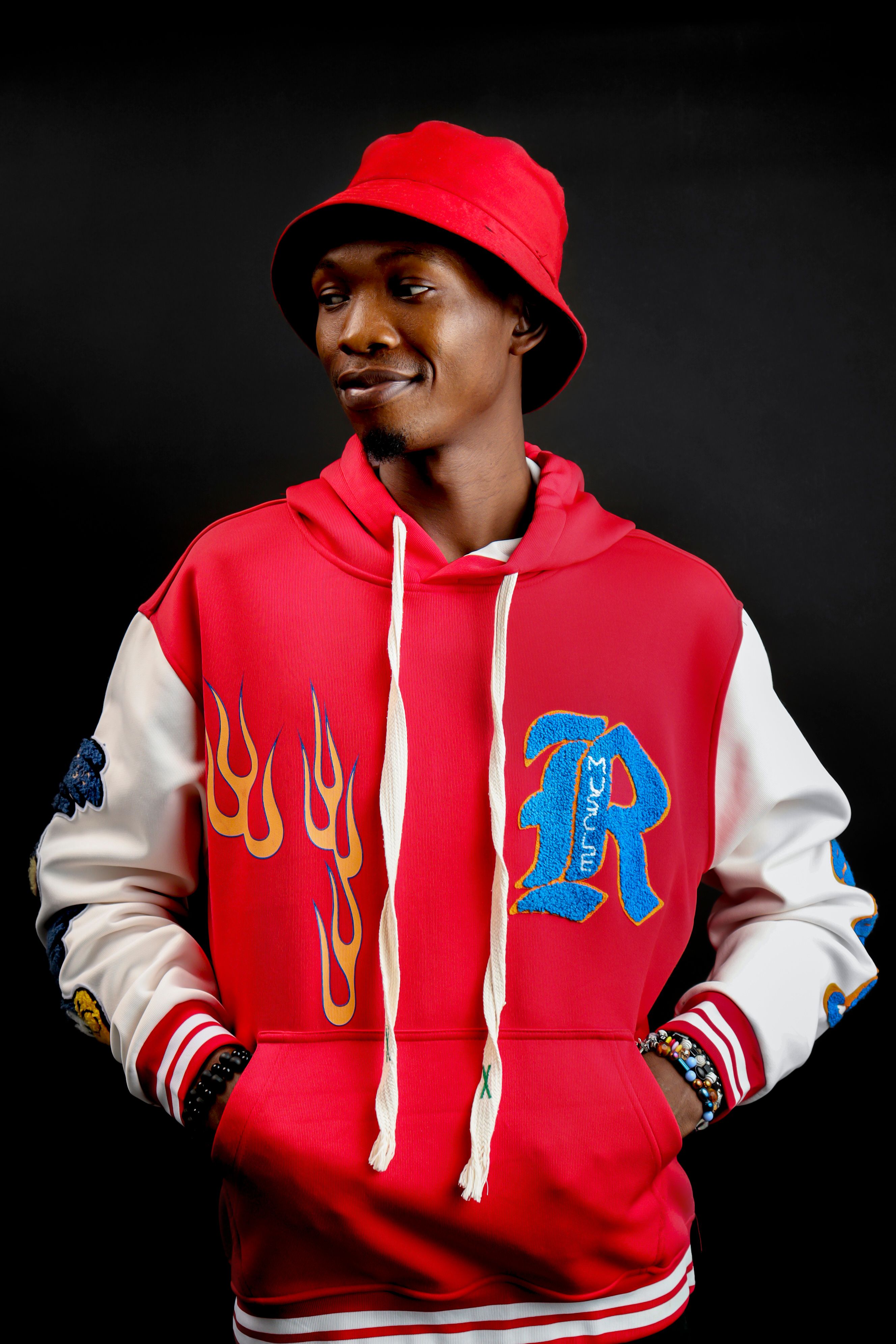 Confident African American man in a studio wearing a red jacket and bucket hat.