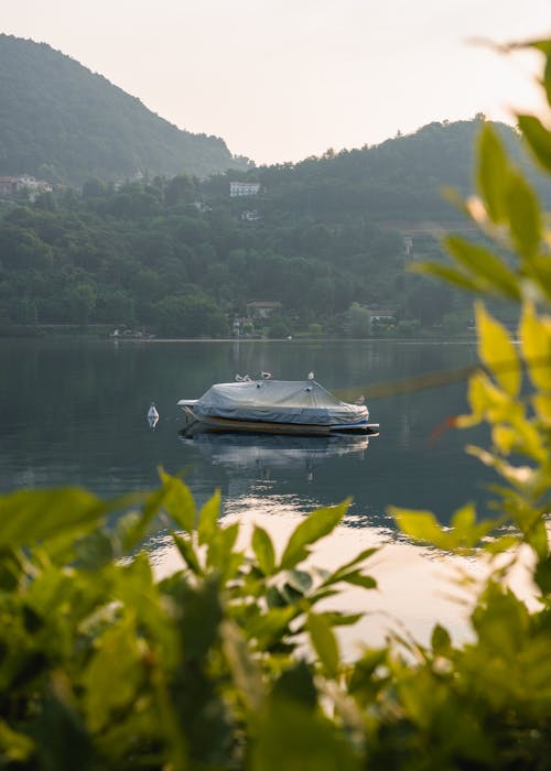 Lonely covered boat sailing on still peaceful water of remote lake among hills in greenery