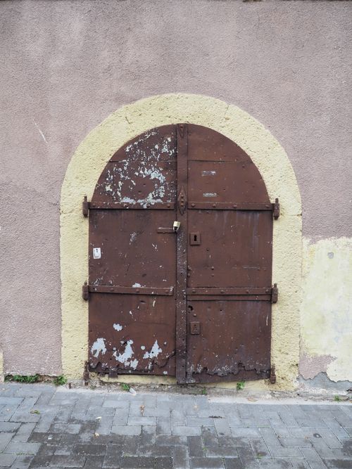 Free Close-up of a weathered arched metal door set in a textured wall, offering a vintage aesthetic. Stock Photo