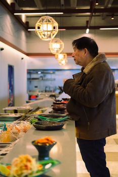 A man with short black hair stands at a restaurant buffet counter with various dishes.