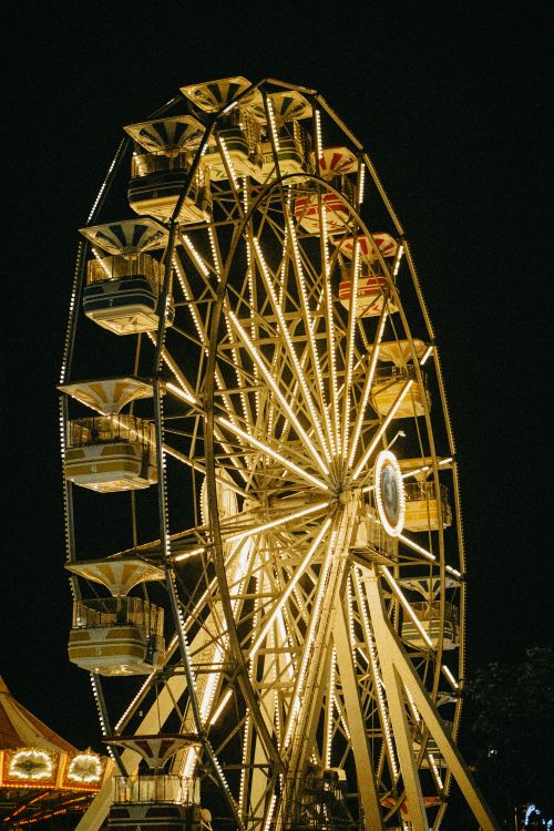 Free A beautifully lit ferris wheel shining bright against the dark night sky at a carnival. Stock Photo