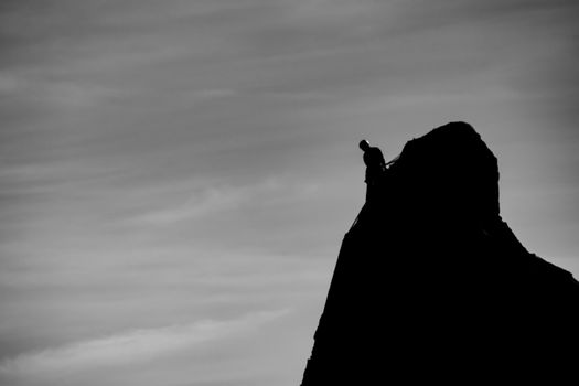 Silhouette of a lone climber scaling a jagged cliff against a moody sky.
