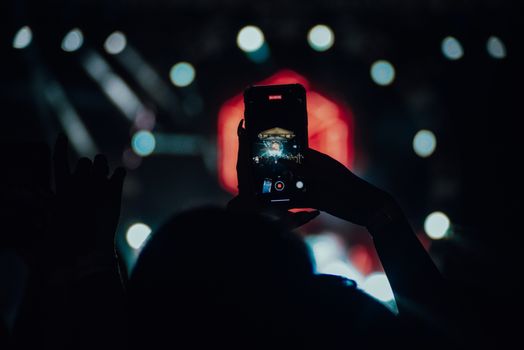 Silhouette using a smartphone to record a live concert scene.