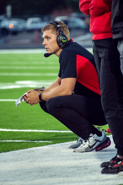 Man in Headphones Squatting by Pitch during Match
