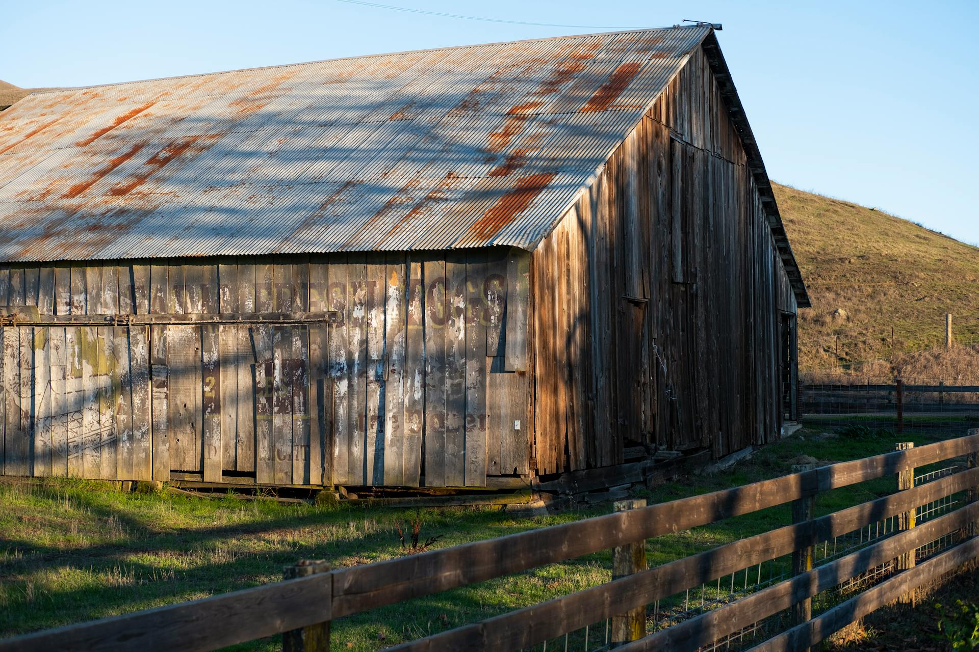 A rustic, weathered barn with a corrugated metal roof in a serene rural setting.