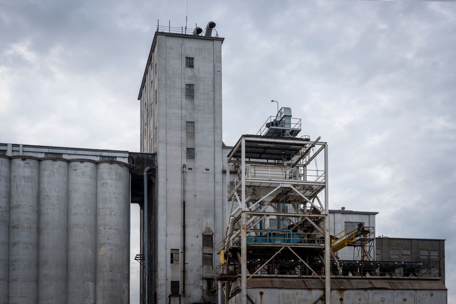 Photograph of a large industrial concrete building with attached silos and machinery under a cloudy sky.