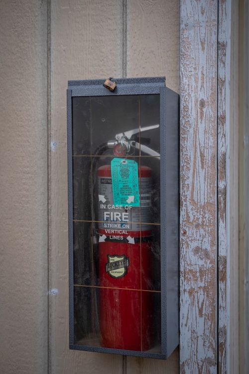 Free A red fire extinguisher enclosed in a glass case mounted on a wooden wall for safety. Stock Photo