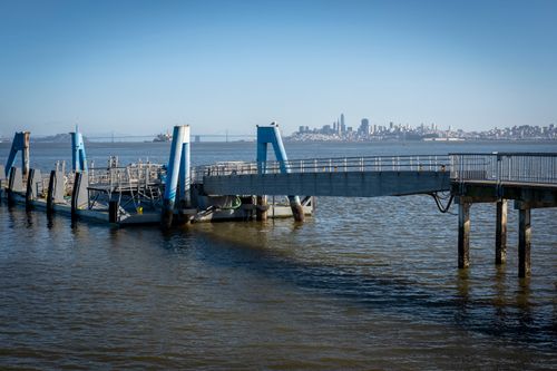 Free A modern jetty extends into San Francisco Bay under a clear blue sky, with city skyline visible. Stock Photo