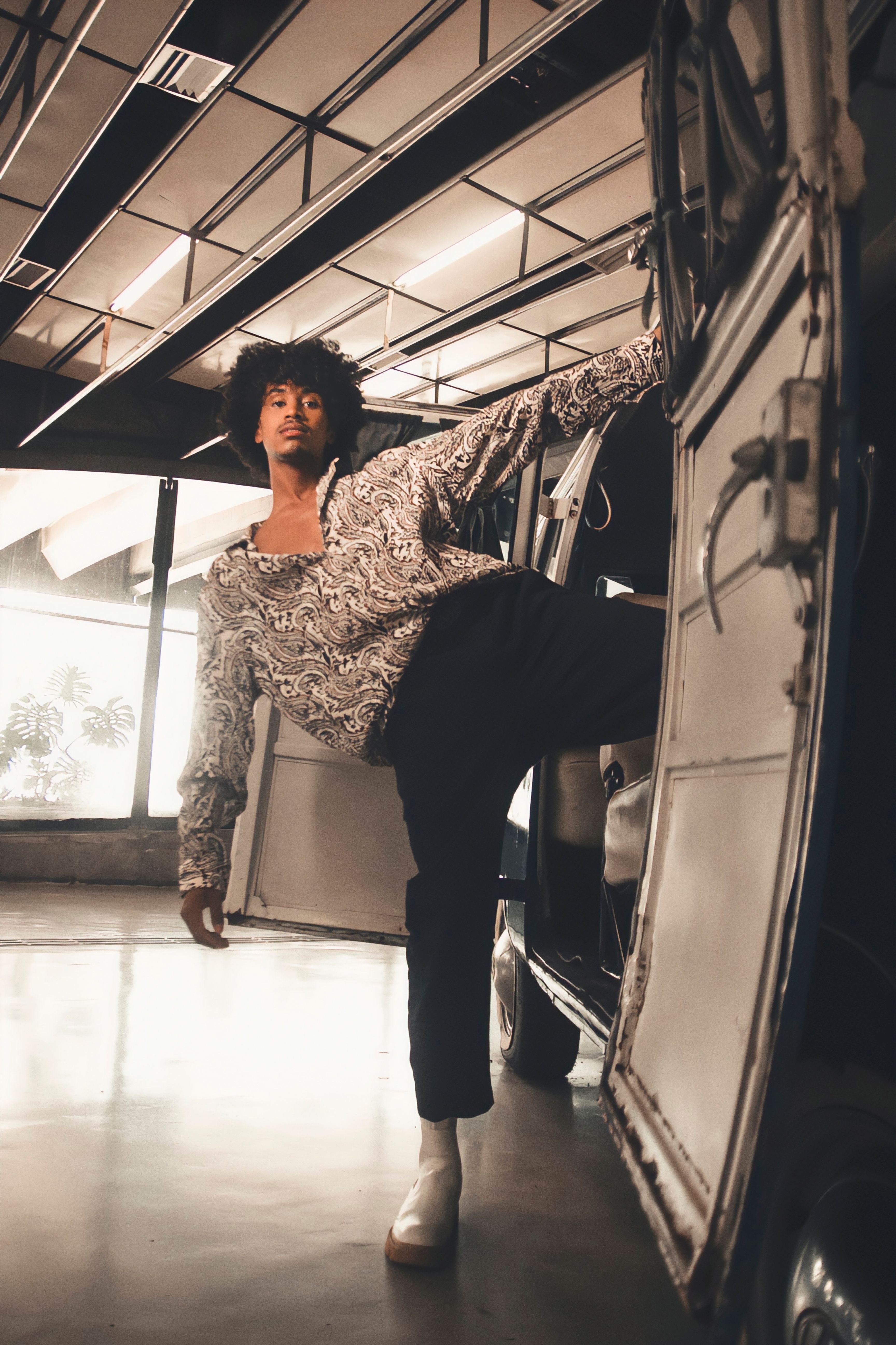 African man models fashionably beside vintage van in modern interior space.