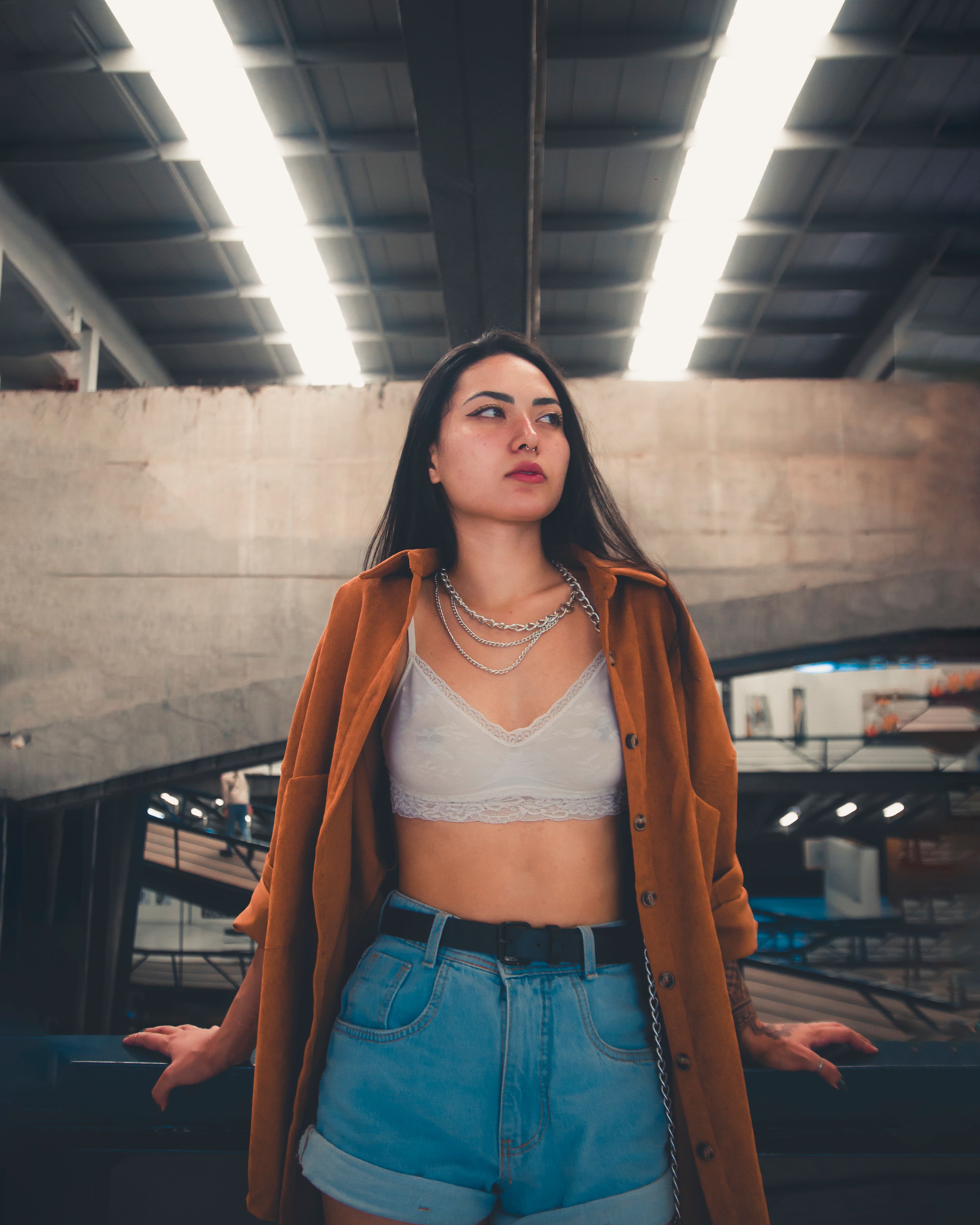 Mulher fashionável em um traje moderno com jaqueta marrom e shorts de jeans dentro de um edifício moderno.