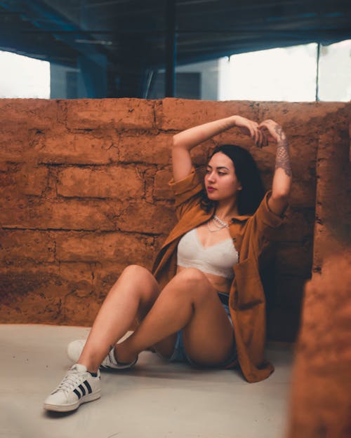 A Woman in White Bra and Brown Long Sleeves Posing Beside the Brown Concrete Wall