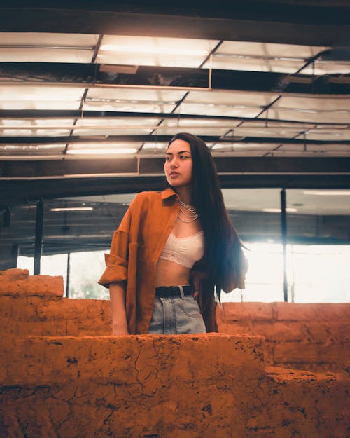 A Woman in White Bra and Brown Long Sleeves Posing Beside the Brown Concrete Wall