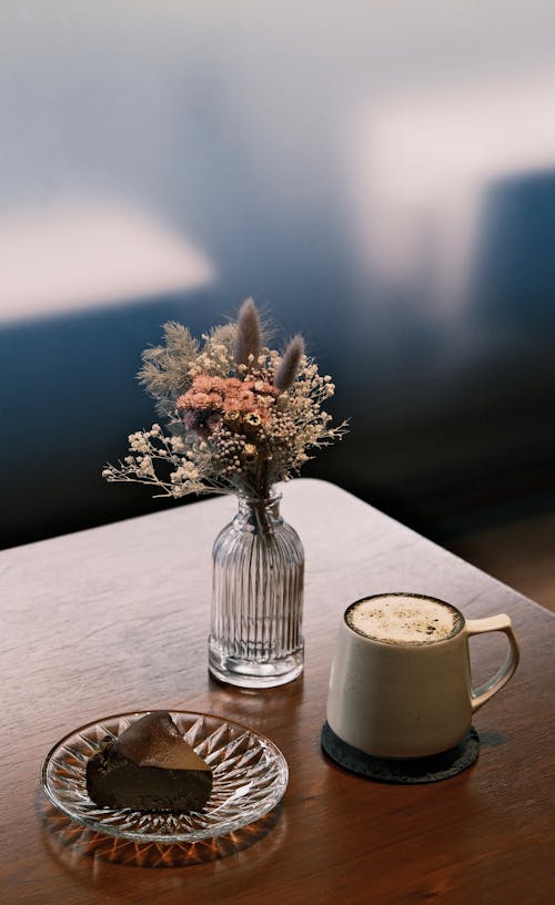 Mug of Coffee, a Slice of Chocolate Cake and a Vase with Wildflowers Lying on a Coffee Table