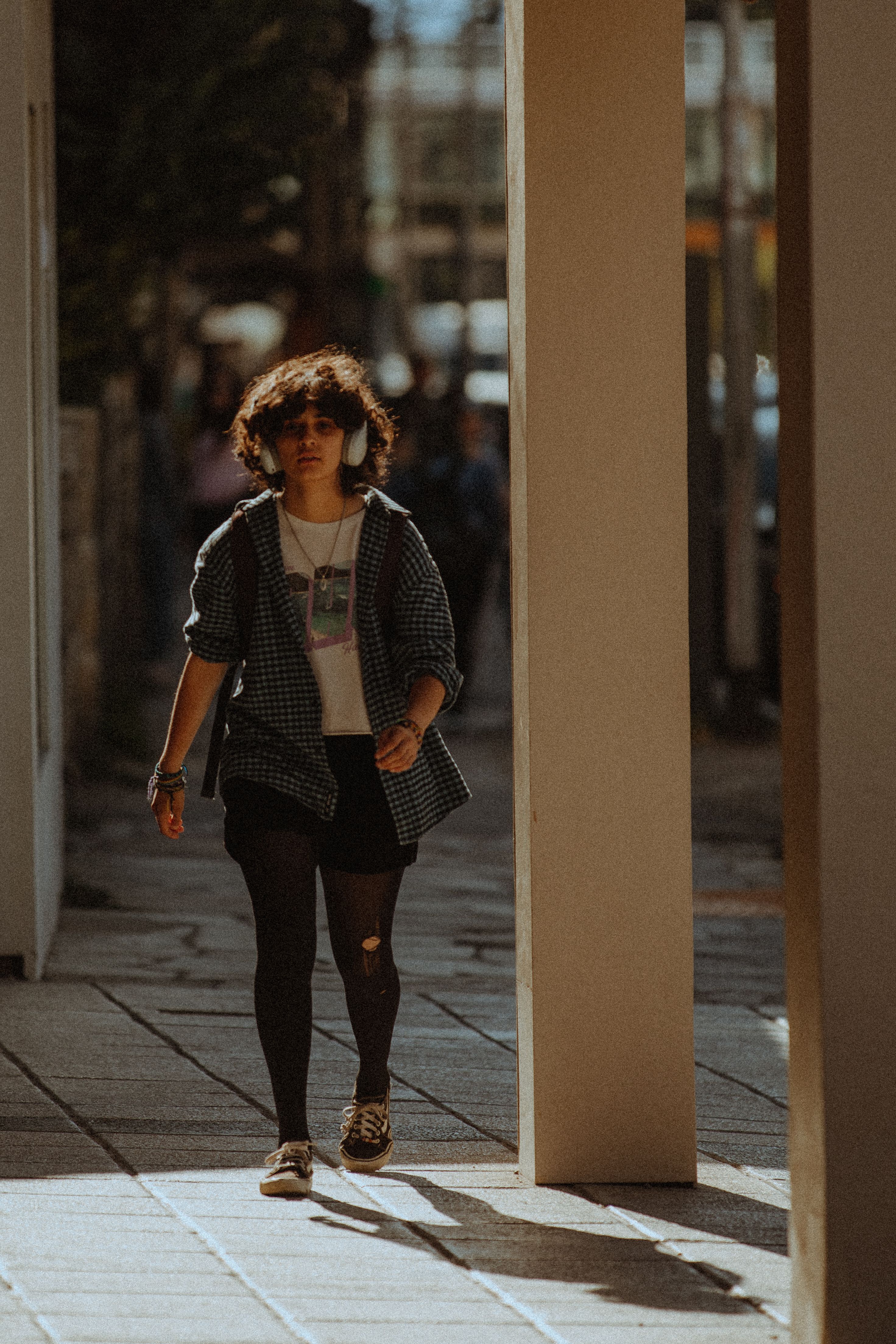 Young woman in casual streetwear walking on a city sidewalk wearing headphones.