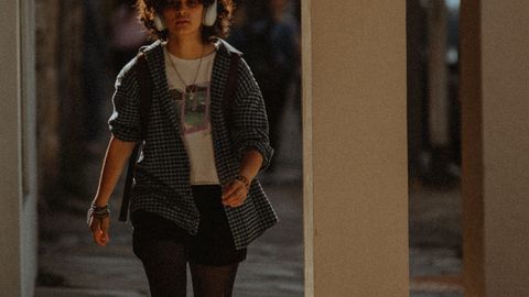 Young woman in casual streetwear walking on a city sidewalk wearing headphones.