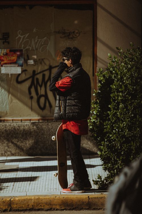 Free Man in a black jacket holding a skateboard, standing on a graffiti-lined street. Stock Photo