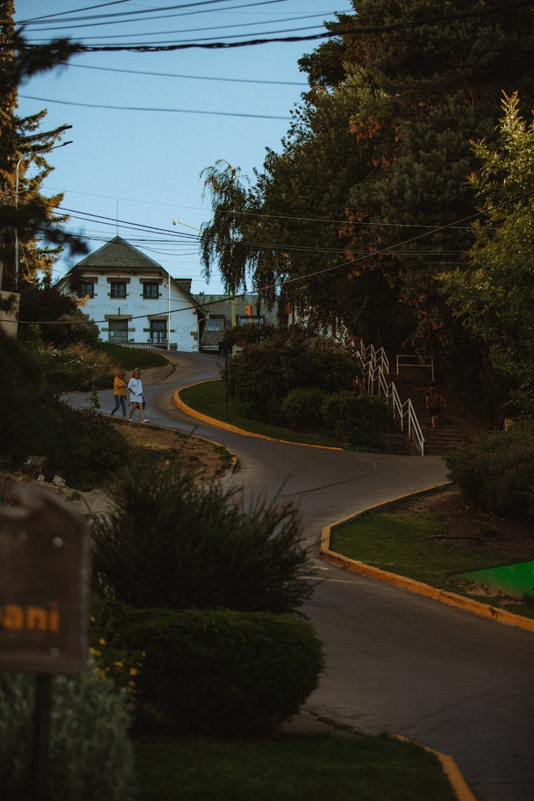 Two People Walking On Downhill Road