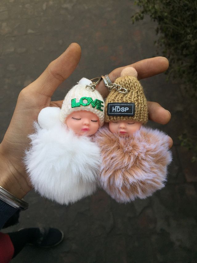 Two fluffy sleeping-doll pom keyrings held in a hand — photo by Sahil Sharma on Pexels