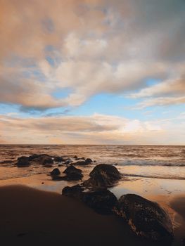 Beautiful rocky shoreline at sunset with calm ocean waves and dramatic clouds.