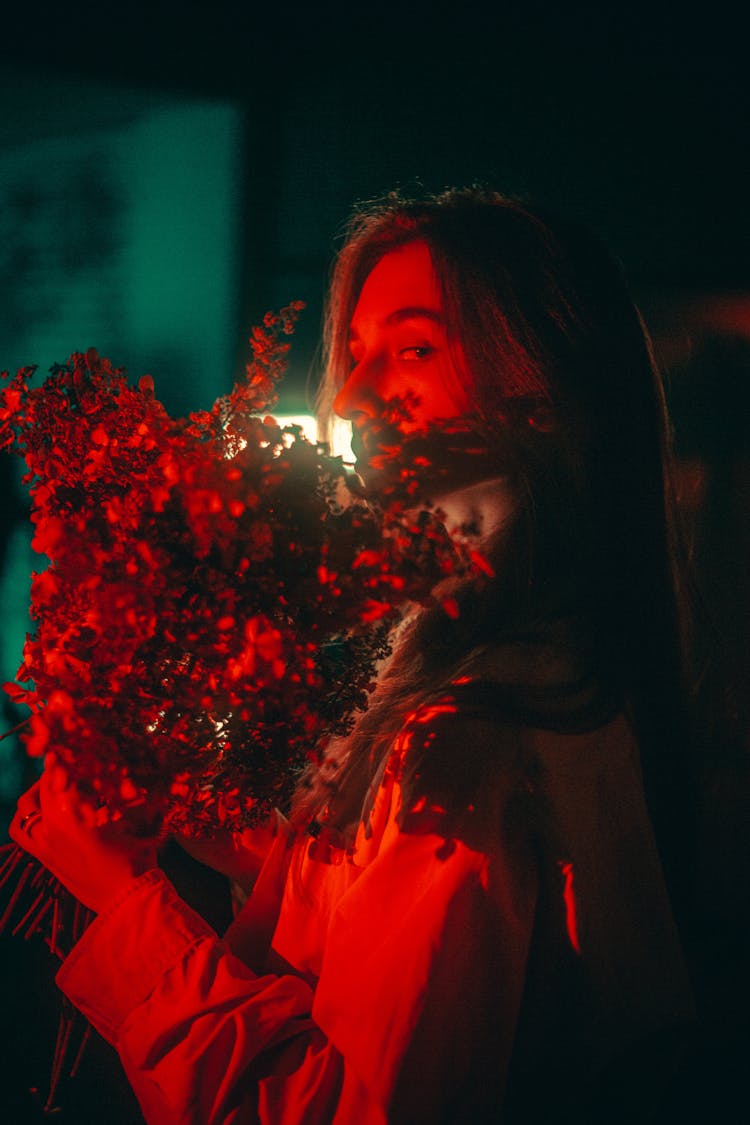 Woman In Red Light Holding A Bunch Of Flowers At Night