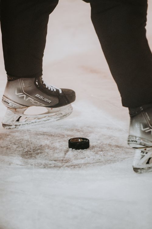Free Close-up of ice hockey skates poised above a puck on the rink. Perfect for sports enthusiasts. Stock Photo
