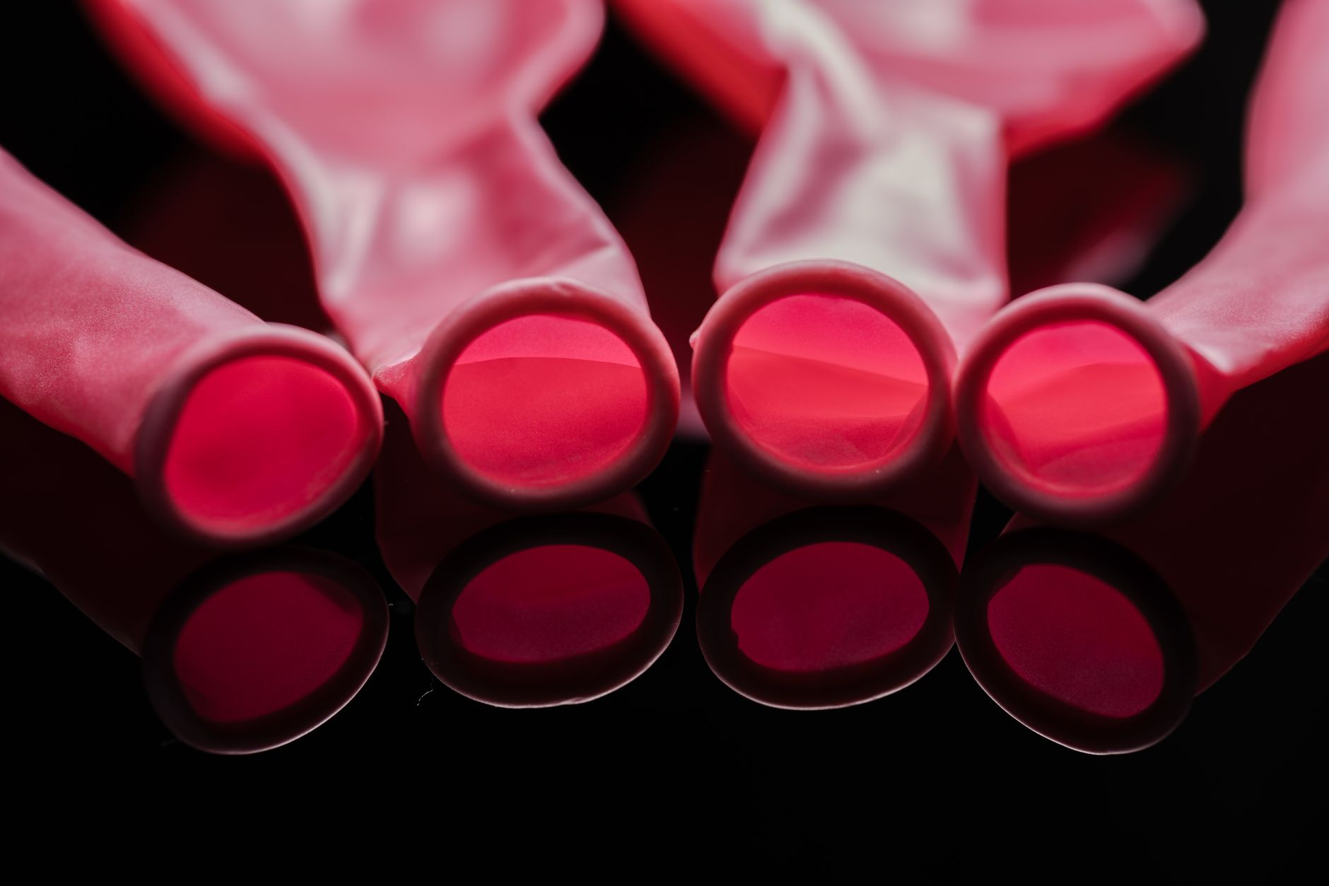 Artistic close-up of pink balloons on a black surface, creating a vivid reflection.