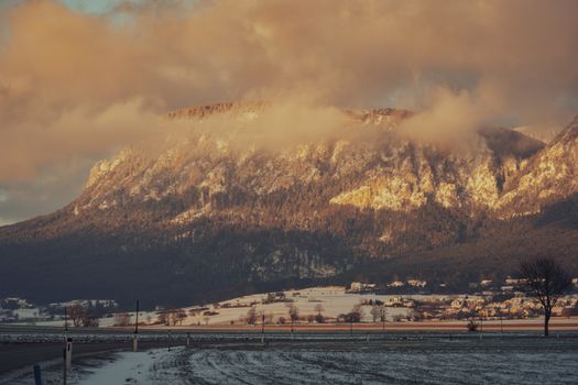 Stunning sunset over snow-dusted mountains and valley with cloud formations.