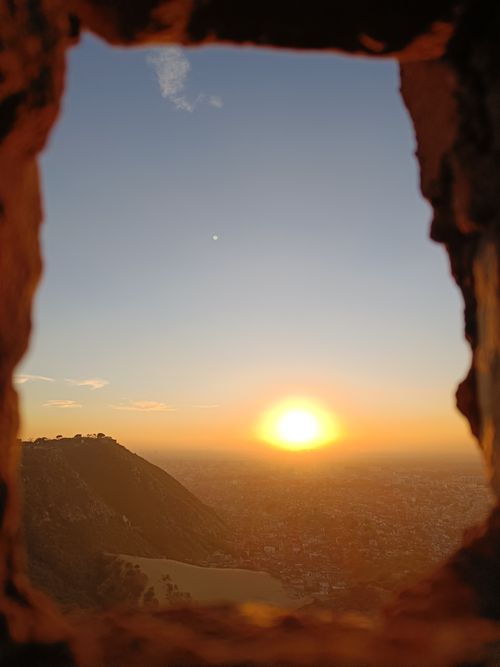 Free A beautiful sunset captured through a stone frame with a scenic view over hills and a distant town. Stock Photo