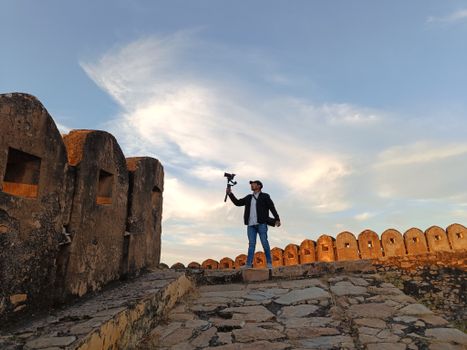 A man capturing video on a fort walkway with a beautiful sky in the background.
