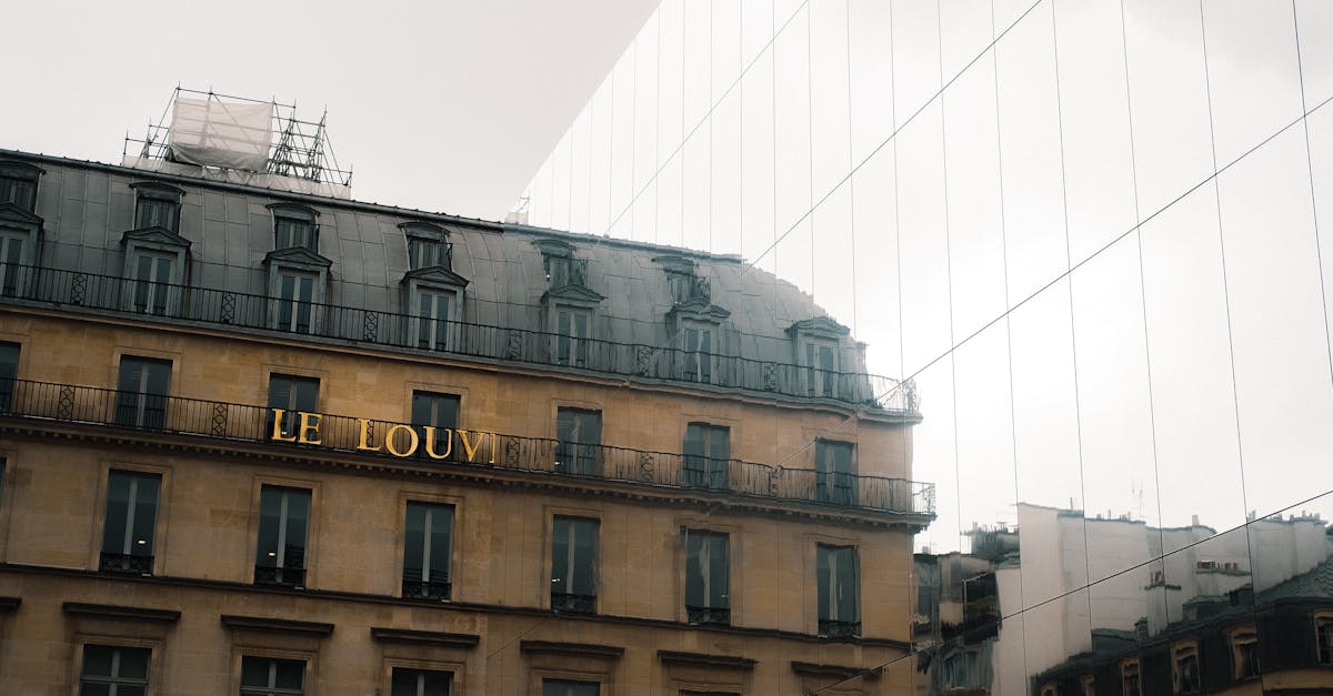 Historic Parisian building reflects on modern glass wall with cloudy sky.