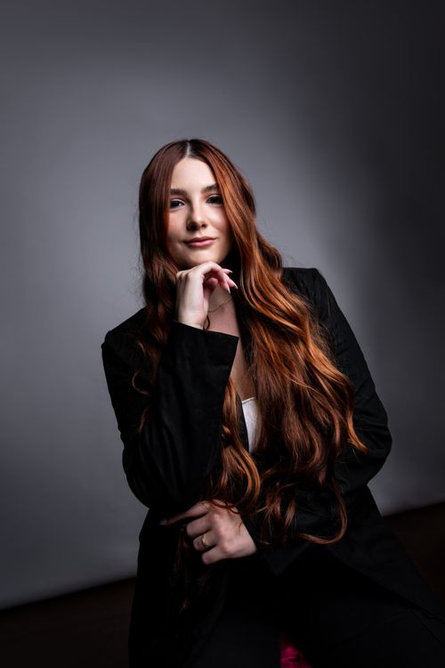 Free Portrait of a woman with long brown hair in a black suit seated against a gray background. Stock Photo