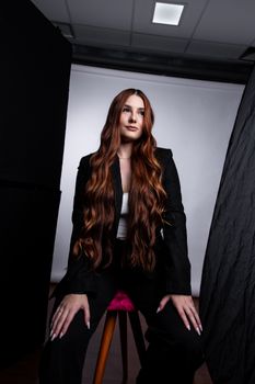 Portrait of a woman in a black suit, sitting confidently in a studio setting.