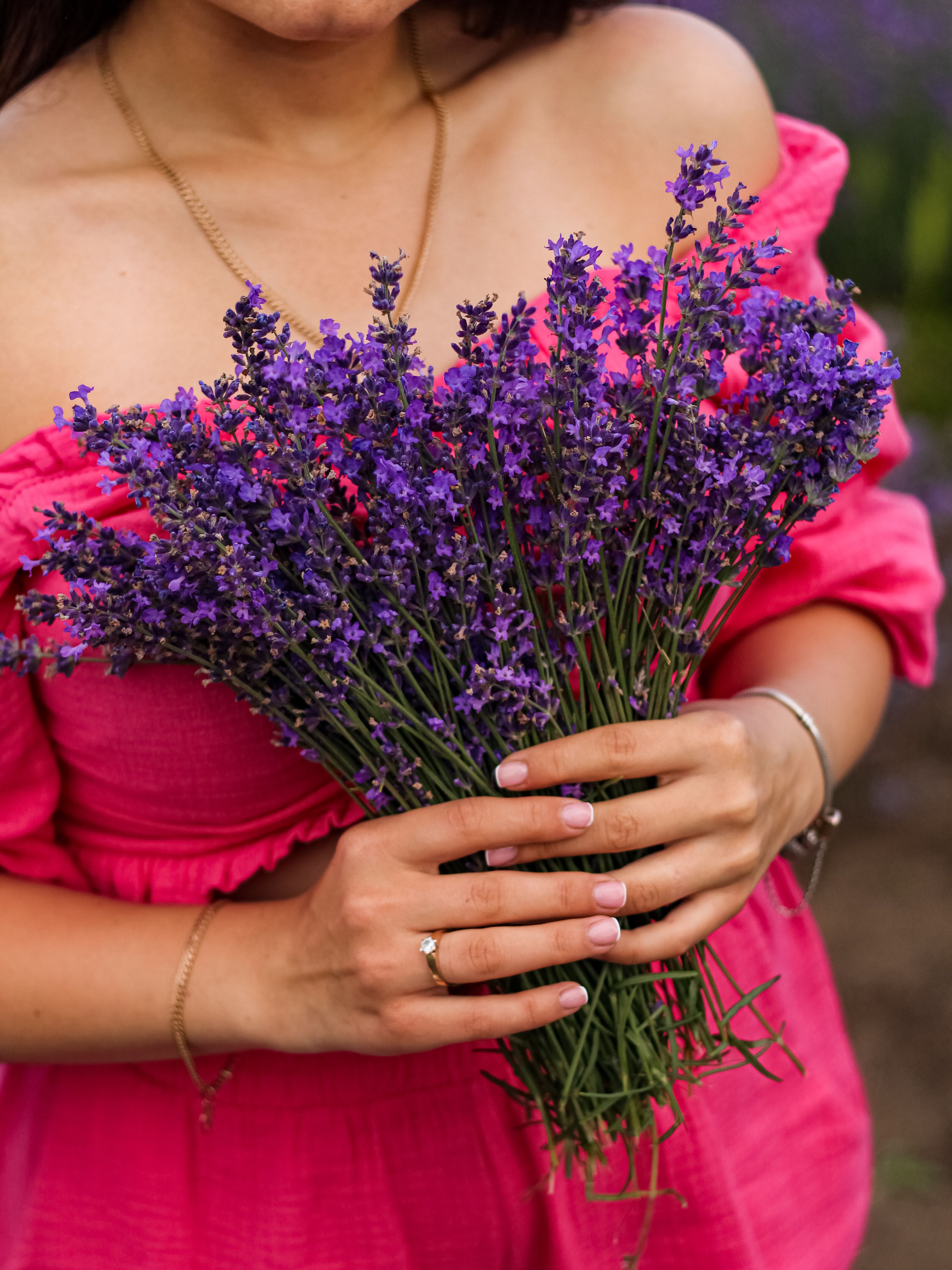 Close-up of a woman holding lavender bouquet while wearing a pink dress, outdoors.