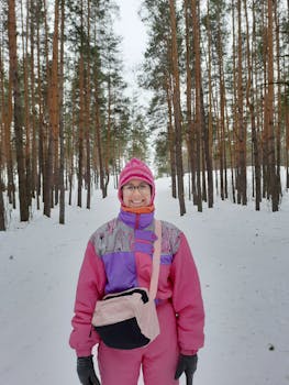 A smiling woman wearing vibrant winter clothing stands in a snowy forest, showcasing a cheerful winter scene.