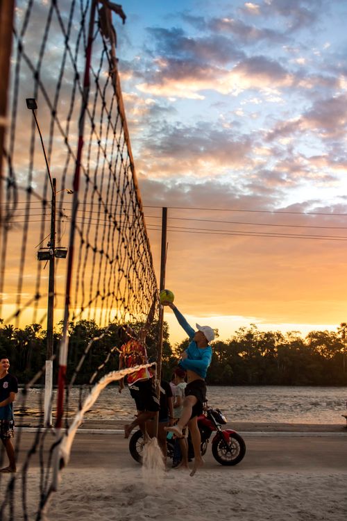Free Men playing volleyball at sunset on a beach, with a motorcycle in the scene. Stock Photo