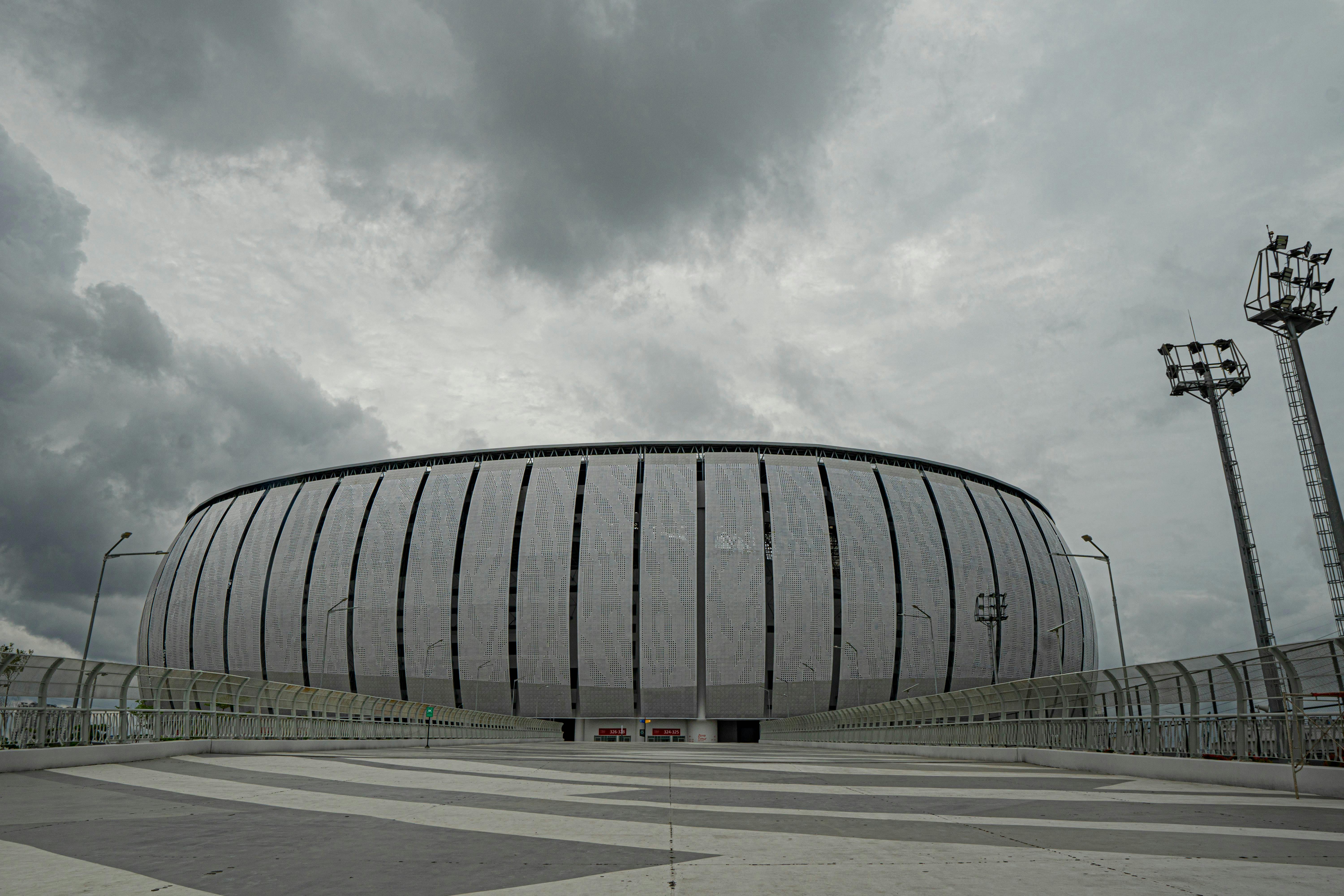 Panoramic view of Jakarta International Stadium with dramatic cloudy skies above, showcasing modern architecture.