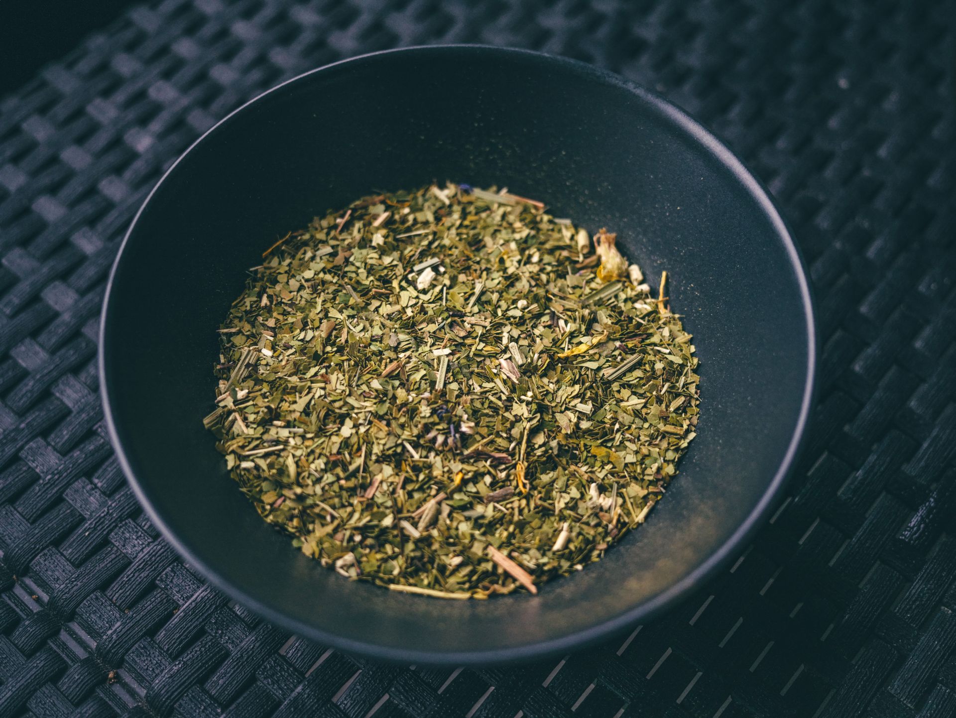 Fresh green herbs in a black bowl on a textured dark mat. Perfect for culinary and cooking themes.