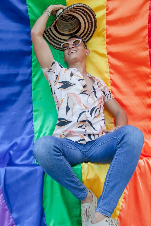 Man in Printed Shirt with Straw Hat Sitting on a Rainbow Flag
