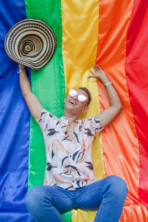 Smiling Man in Printed Shirt with Straw Hat Sitting on a Rainbow Flag