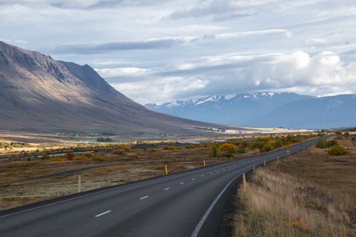 Free A tranquil road stretches through a picturesque valley with gentle mountains and cloudy skies. Stock Photo