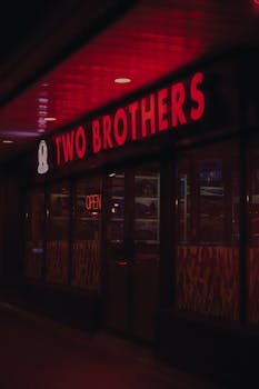 Moody night scene of a red neon-lit restaurant sign reading 'Two Brothers'.