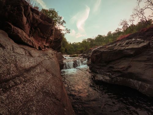 Free Beautiful waterfall cascading through rocky formations, surrounded by lush greenery under a clear blue sky. Stock Photo