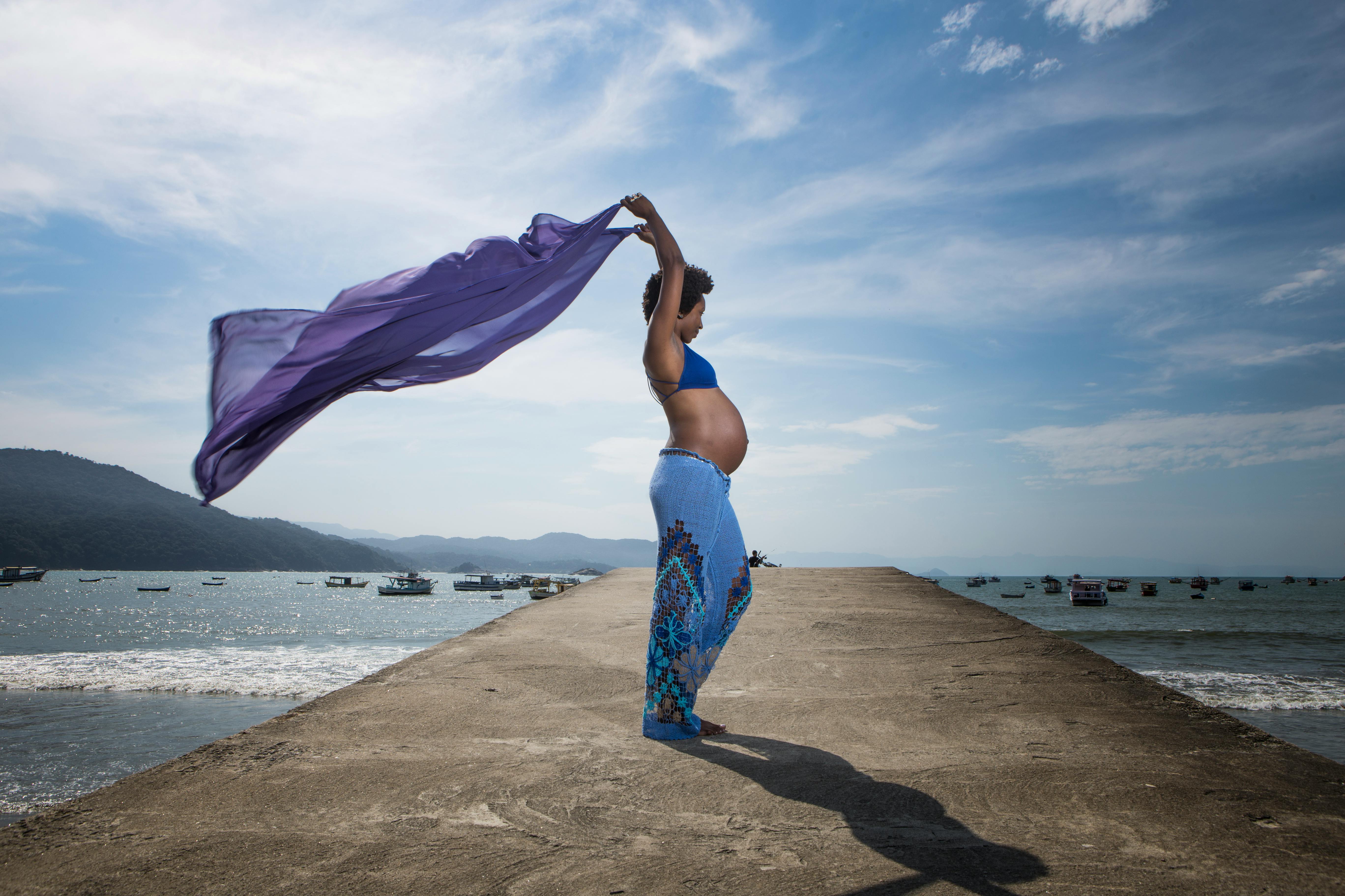 a pregnant woman is standing on a pier with her arms outstretched