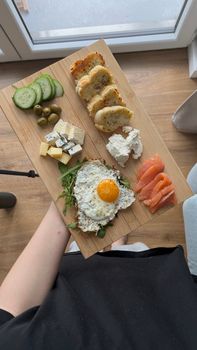 Top view of a breakfast platter featuring fried egg, cheese, salmon, and bread on a wooden board.