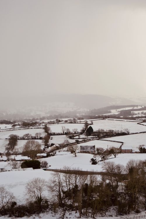 Free Drone shot of a rural countryside covered in snow during winter, showcasing a serene landscape. Stock Photo