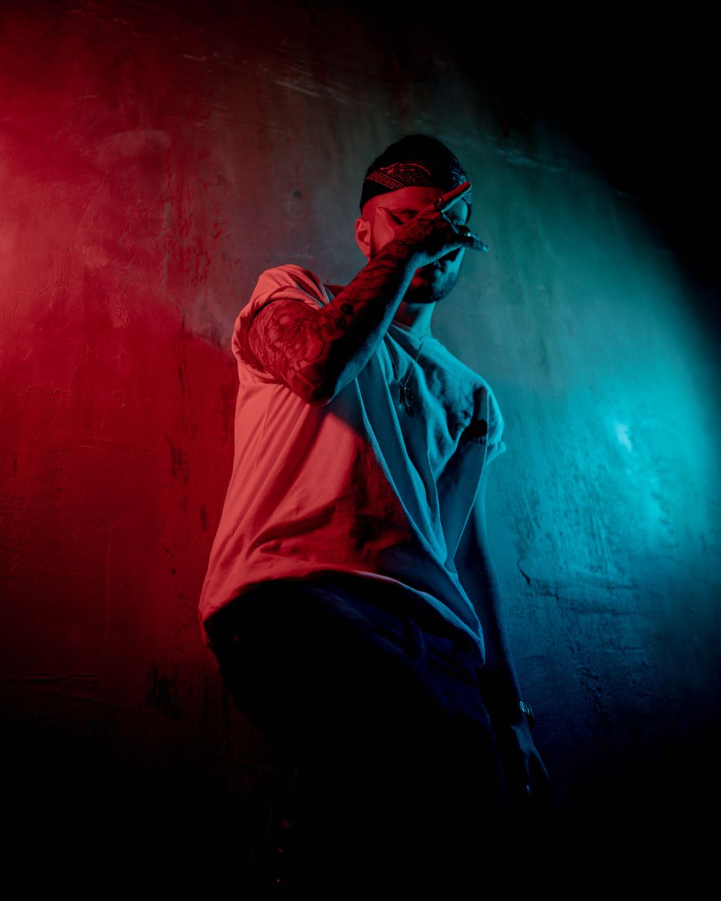 A dramatic portrait of a man highlighted in vivid red and blue lighting, captured in a moody atmosphere.