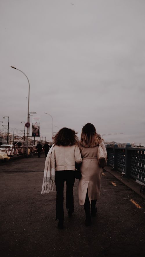 Free Two women walking arm in arm on Galata Bridge, Istanbul under overcast skies. Stock Photo